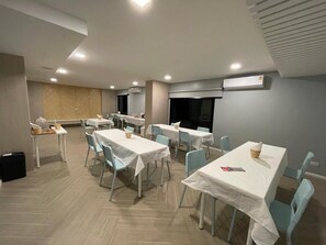 Comedor con varias mesas y sillas, unidades de aire acondicionado y una pared con motivo de espiga.