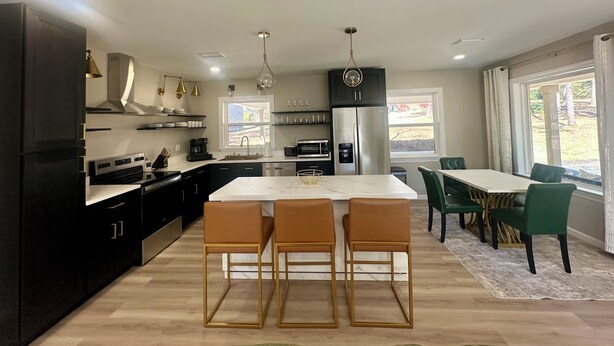 Una cocina moderna con una isla central, armarios negros, electrodomésticos de acero inoxidable y una zona de comedor con sillas verdes.