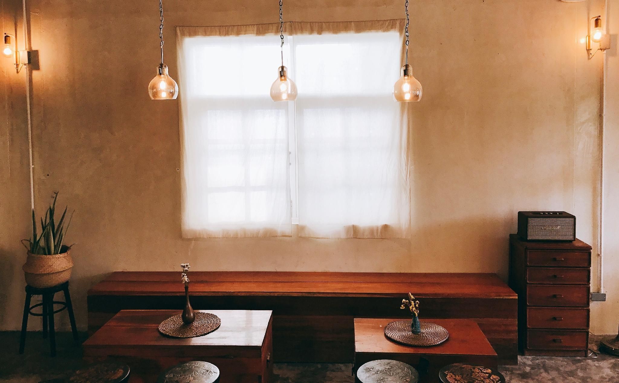 Un cuarto acogedor con un banco de madera, dos mesitas con jarrones decorativos, una planta en maceta y una radio antigua sobre un mueble de madera.