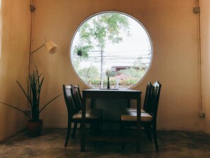 Taula rodona amb quatre cadires, una planta en test i una làmpada de peu en una habitació amb un finestral gran.