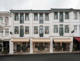 Un edificio blanco con contraventanas verdes y una cafetería en la planta baja.