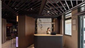 A reception desk with a modern design, a person seated behind it, and a view of the outside through large windows. - Claude Hotel (Singapore)