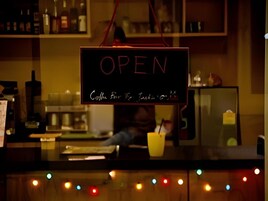 Bancada de bar com um letreiro de neon 'OPEN', uma máquina de café e uma xícara amarela.