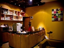 Uma área de bar com prateleiras de garrafas, uma máquina de café e um balcão com bancos.