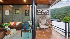 Une pièce chaleureuse avec un plafond en bois, un canapé agrémenté de coussins colorés, un fauteuil en osier et une vue sur un paysage verdoyant luxuriant.