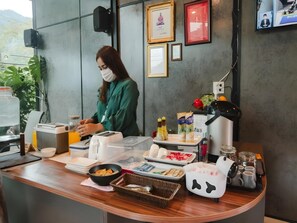 A counter with food items, a coffee machine, and a person wearing a mask. - The Sky Roof Homestay Kiriwong (Lan Saka)