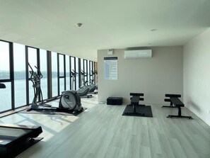 Ein Fitnessraum mit Cardiogeräten, Bänken und Blick auf ein Gewässer.