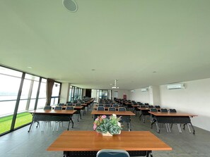Ein Konferenzraum mit mehreren Tischen und Stühlen, großen Fenstern und einer Klimaanlage an der Wand.