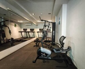 Une salle de sport équipée de tapis de course, d’appareils de musculation et d’un mur recouvert de miroirs.