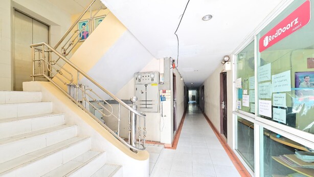 A hallway with a staircase, a RedDoorz sign, and a glass display case with papers. - Big Bird Palace (Bangkok)