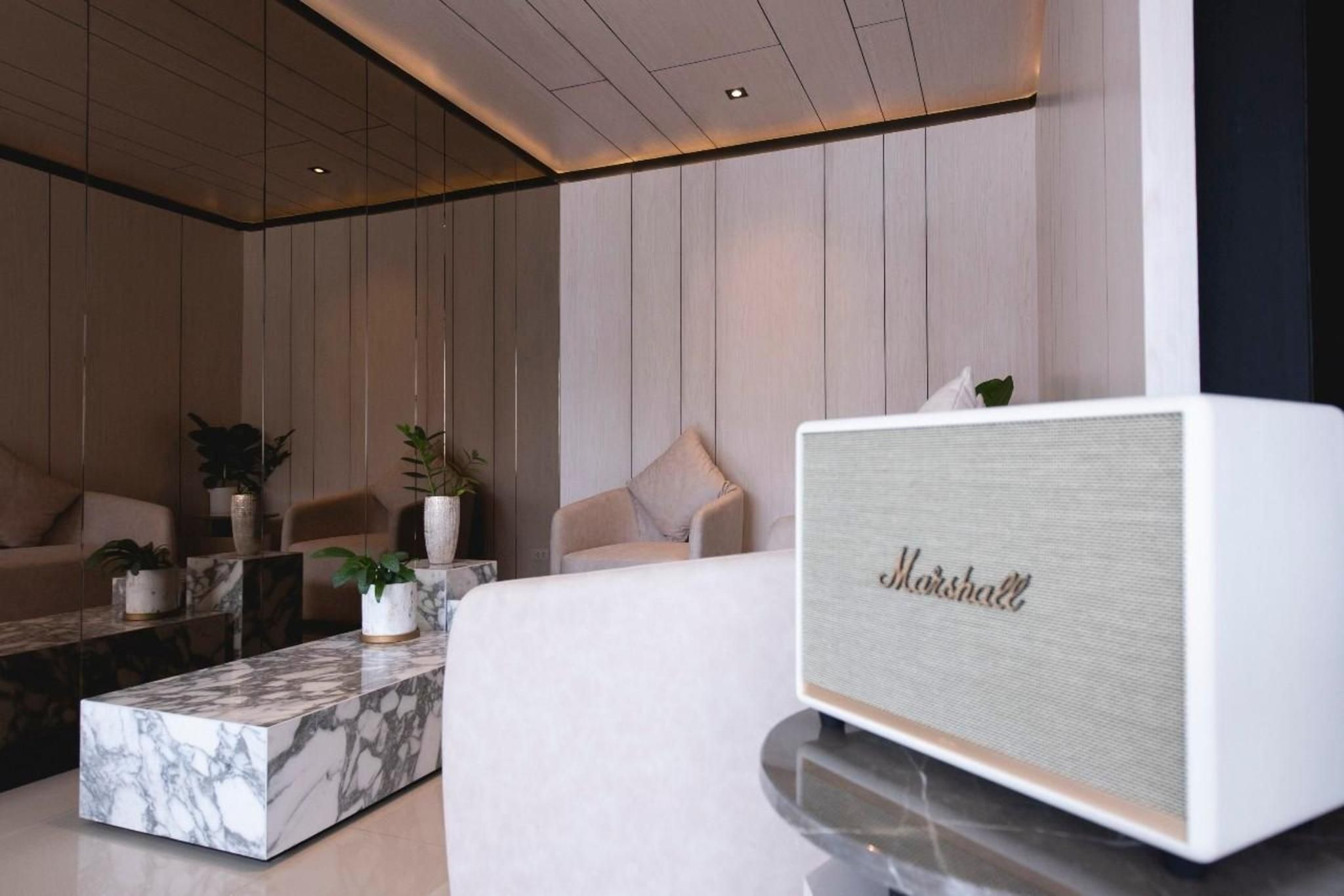 A modern living room with a marble coffee table, beige sofas, and a white Marshall speaker.