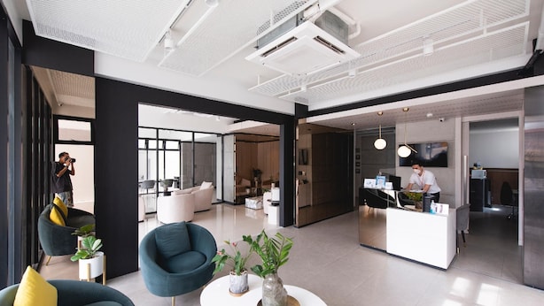 A modern hotel lobby with a reception desk, seating area with armchairs, and a large window providing natural light. - Qlosest Hotel (Nakhon Ratchasima)