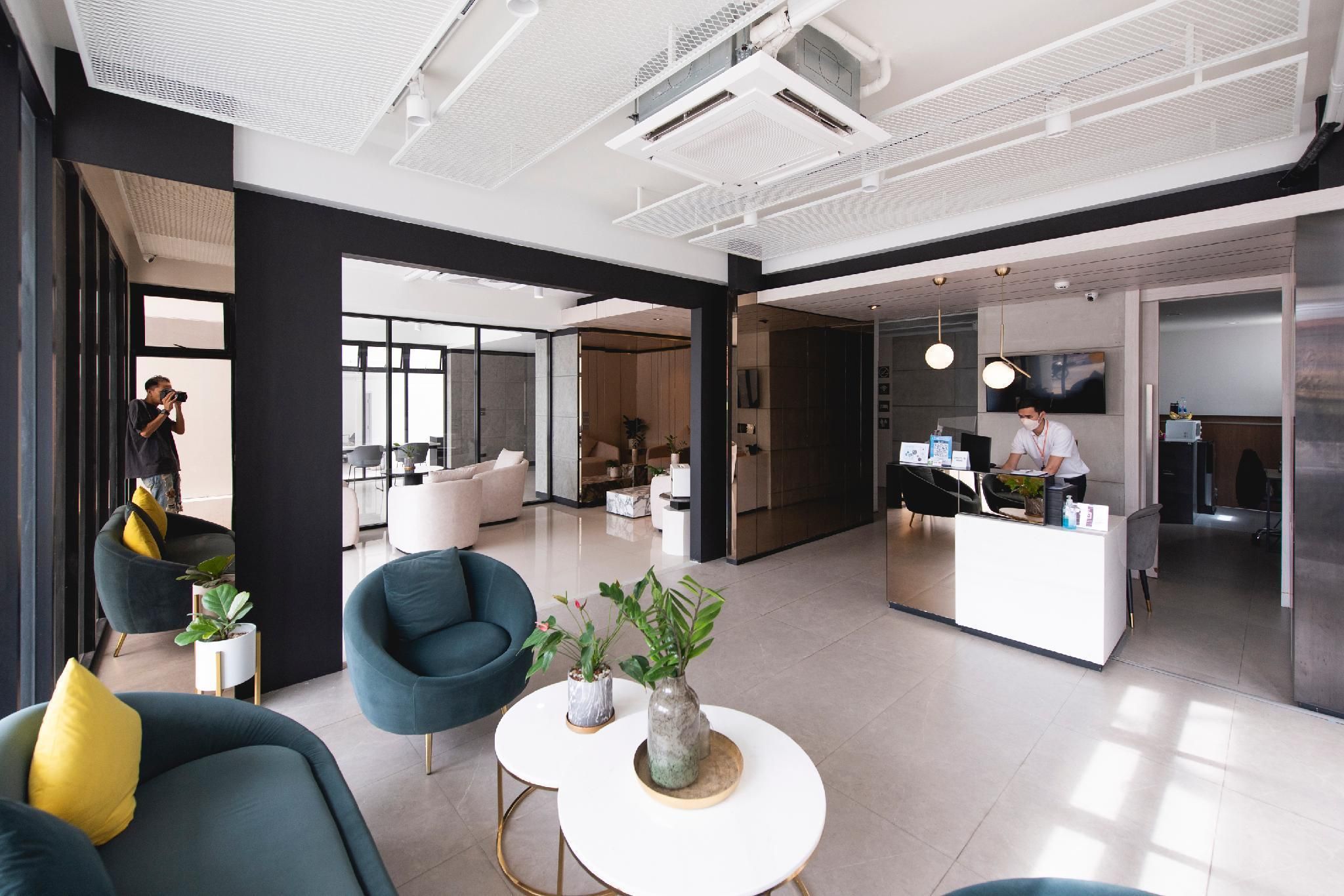 A modern hotel lobby with a reception desk, seating area with armchairs, and a large window providing natural light.