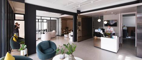 A modern hotel lobby with a reception desk, seating area with armchairs, and a large window providing natural light.