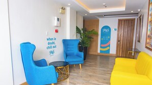 A hotel lobby with blue armchairs, a yellow sofa, a potted plant, and a wall with a slogan. - Luxebridge Hotel (Davao)