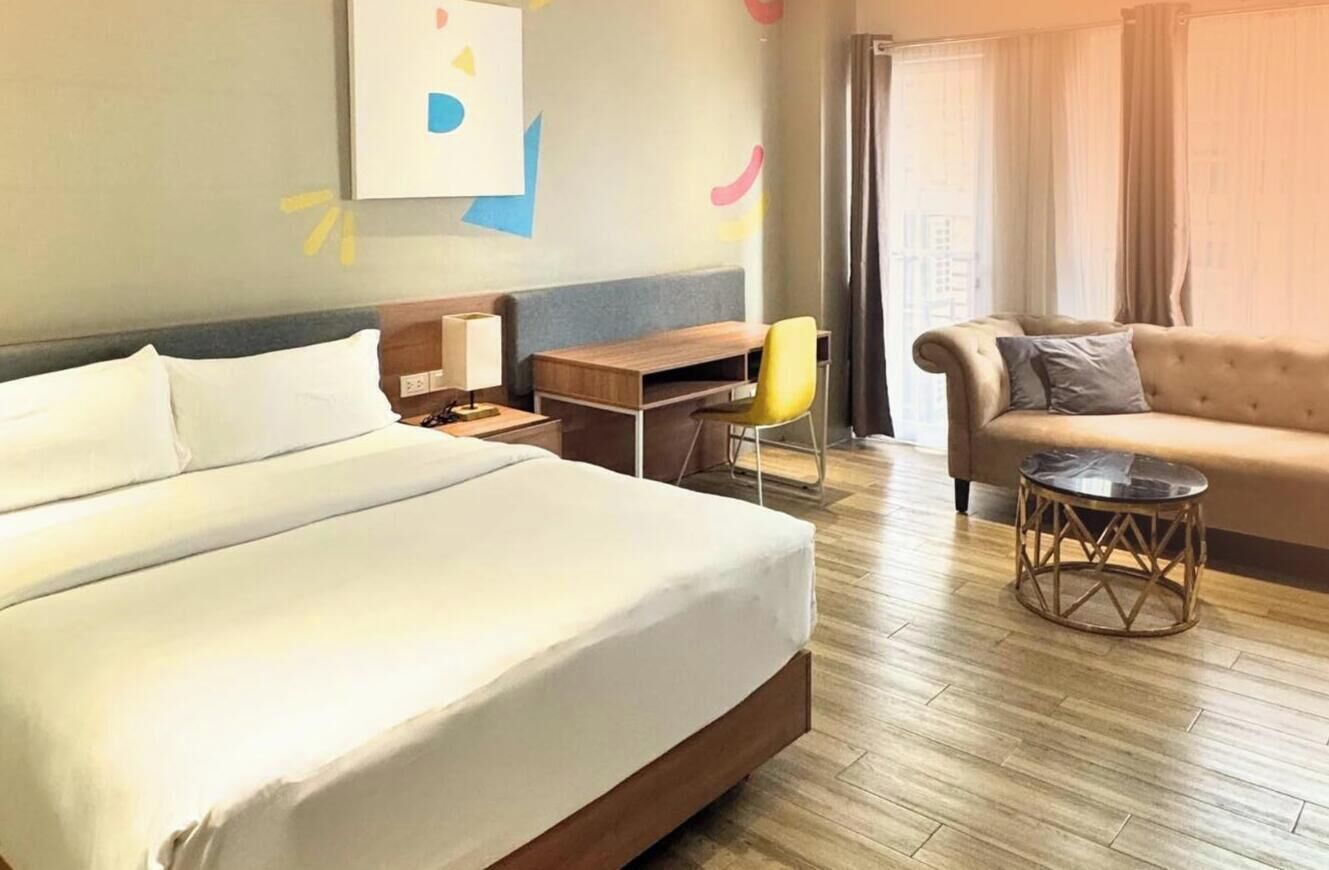 A hotel room with a large bed, a desk, a chair, a sofa, and a small round table.