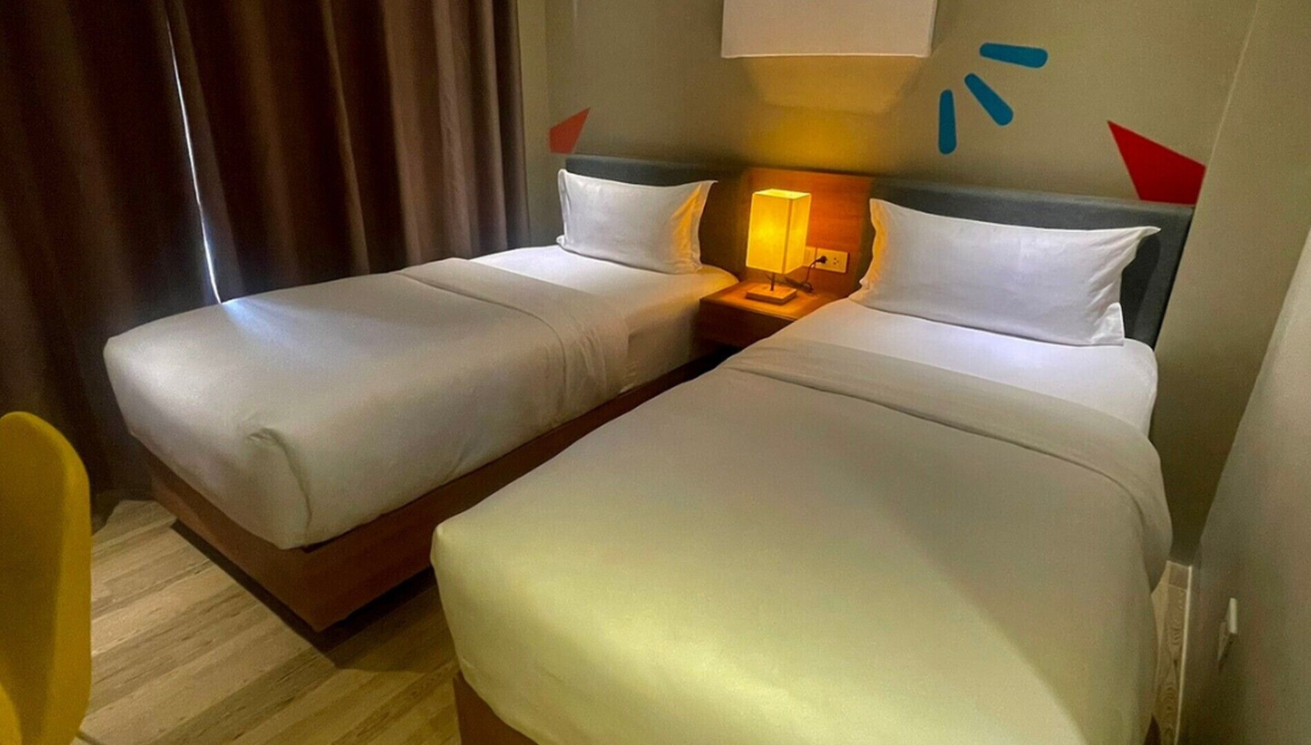 Ein Hotelzimmer mit zwei Einzelbetten, einem Nachttisch mit Lampe und Holzboden.