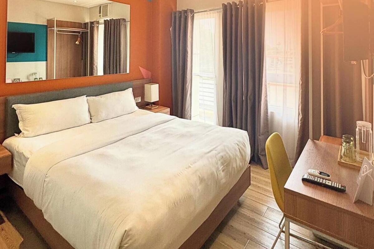 Habitació d'hotel amb un llit gran, un escriptori amb cadira, televisió i un mirall.