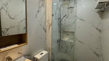 A bathroom with a marble wall, a glass-enclosed shower, and a toilet.