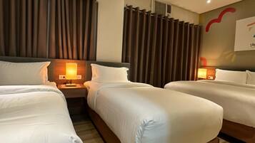 A hotel room with two single beds, a nightstand with a lamp, and a large window with curtains.