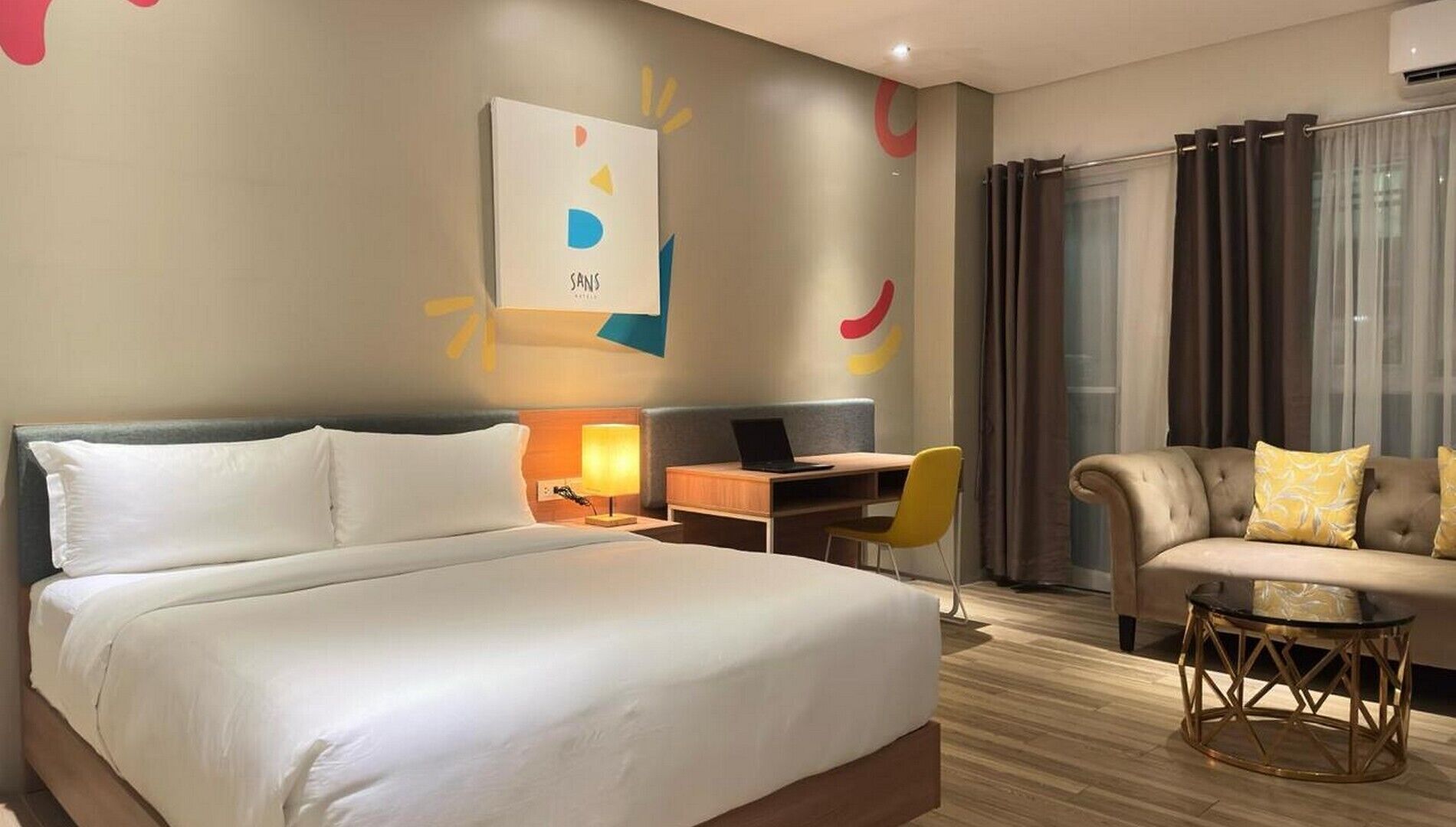 Una habitación de hotel con una cama grande, un escritorio con una computadora portátil, un sofá y una pequeña mesa redonda.