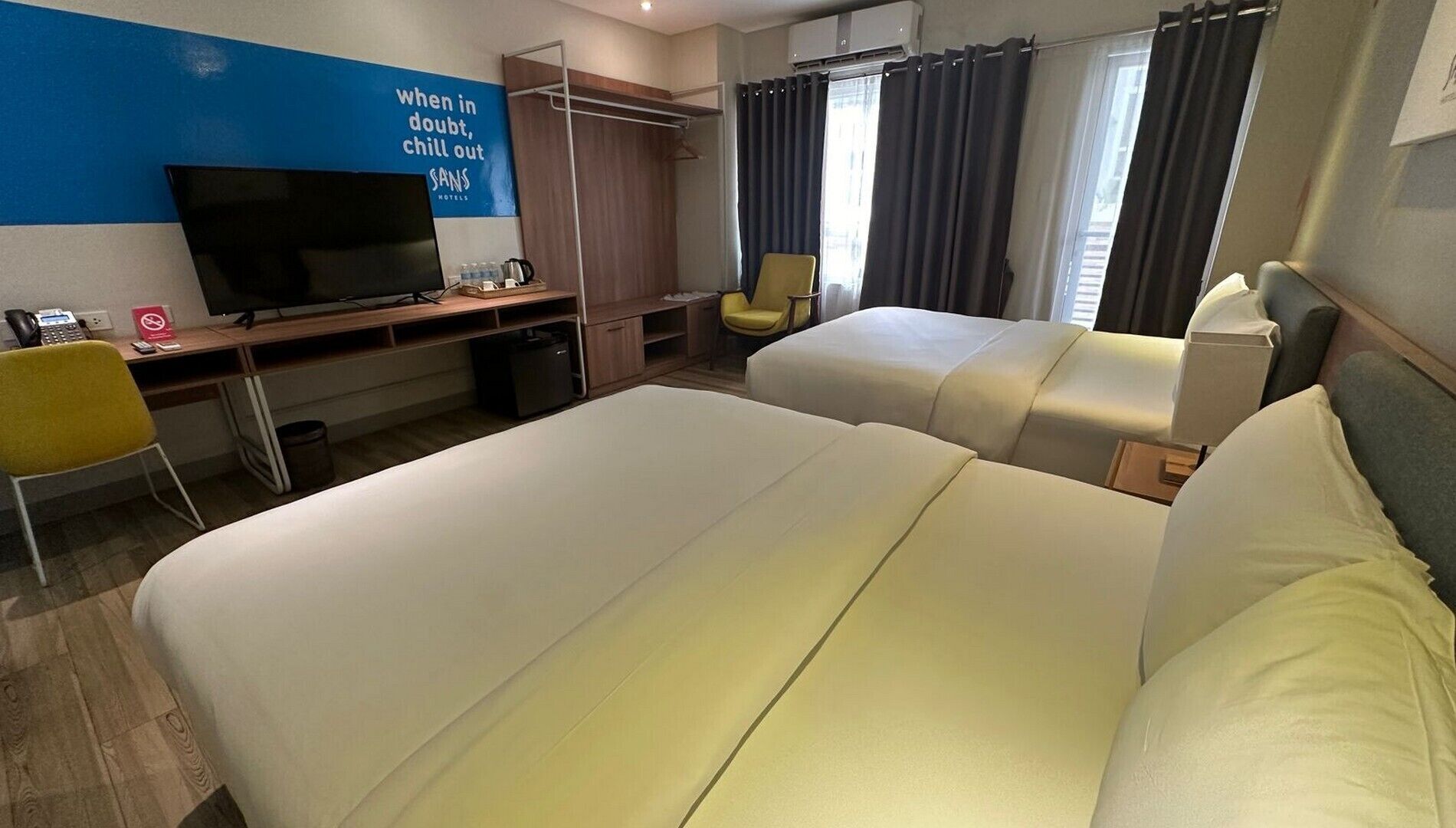A hotel room with two beds, a desk with a computer, a chair, and a TV.