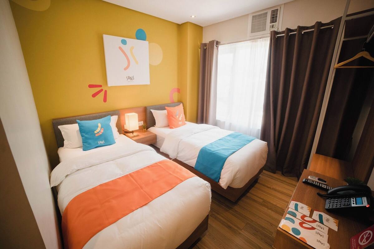 Habitació d'hotel amb dos llits, una vetustat de fusta, un telèfon i una finestra amb cortines.