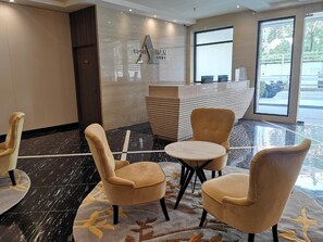 Un hall d’hôtel avec un sol en marbre, un comptoir d’accueil et deux fauteuils confortables.