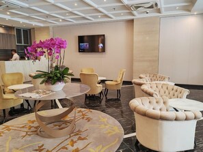 Un hall d’hôtel moderne comprenant un comptoir d’accueil, des sièges confortables, un grand téléviseur et une plante décorative.
