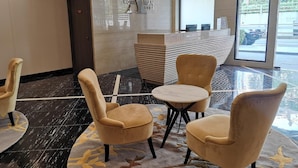 Un hall d’hôtel avec un sol en marbre, un comptoir d’accueil et deux fauteuils confortables.