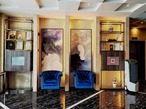 Un hall d’entrée avec deux fauteuils bleus, un comptoir d’accueil orné de certificats encadrés et un mur décoré d’œuvres d’art abstraites.