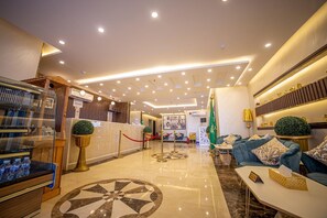 Un hall d’hôtel comprenant un comptoir d’accueil, un espace détente avec des canapés, un distributeur d’eau et un motif décoratif sur le sol.