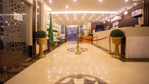 Un hall d’hôtel doté d’un sol en marbre, d’un comptoir d’accueil et d’un mur décoratif orné d’un motif géométrique.