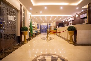 Un vestíbulo de hotel con piso de mármol, un mostrador de recepción y una pared decorativa con diseño geométrico.