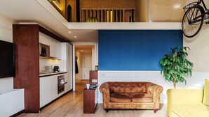 Un espacio habitable moderno con cocina, sofá, un sillón amarillo y una planta grande.