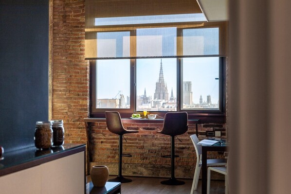 Una habitación con un ventanal amplio que ofrece vistas a la ciudad, una pared de ladrillo y una mesa con sillas.