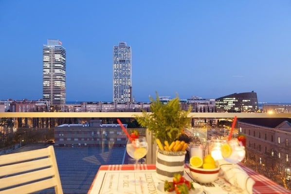 En balkon med et bord dækket til to, med udsigt over bybilledet med moderne bygninger og en havnefront.