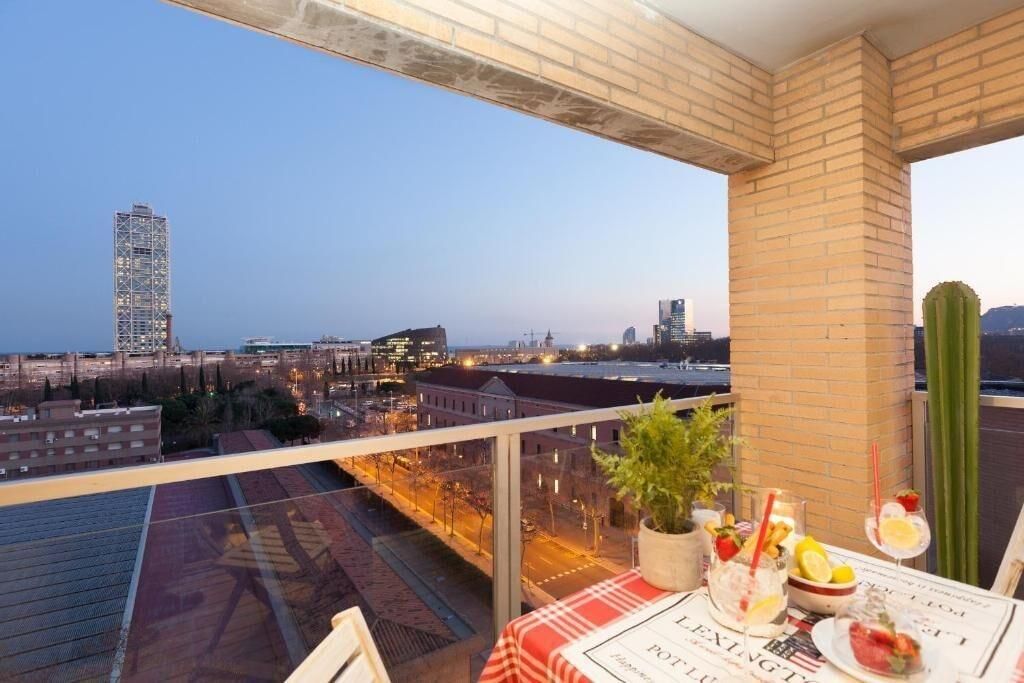 Un balcon avec une table dressée pour le dîner, offrant une vue sur un paysage urbain avec ses bâtiments et un ciel dégagé.