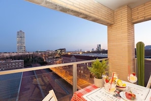 En balkon med et spisebord, udsigt over et bybillede med bygninger og en klar himmel.