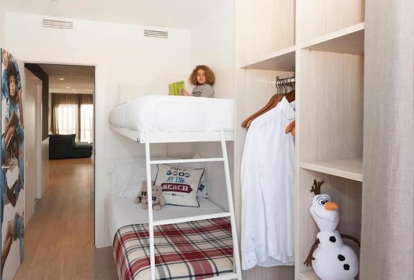 Una cama litera con un niño leyendo, una decoración de muñeco de nieve y un armario con ropa colgada.