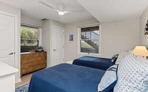 A bedroom with two beds, a dresser, a window with a view of a staircase, and a ceiling fan. - Luxury Lakefront Living | New vacation rental (Spring Lake)