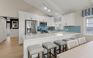 A modern kitchen with white cabinets, a stainless steel refrigerator, a microwave, and a large island with bar stools. - Luxury Lakefront Living | New vacation rental (Spring Lake)