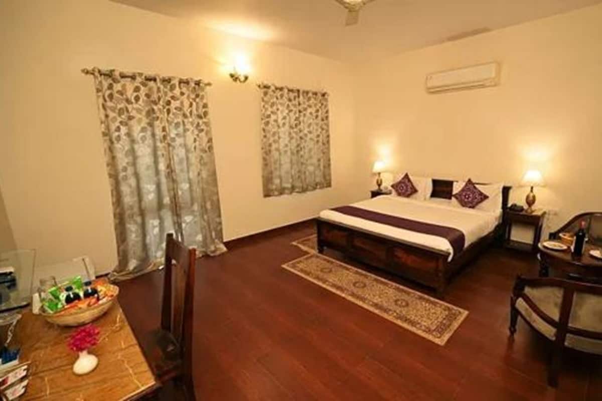 A hotel room with a wooden bed, two bedside tables with lamps, a chair, a small table with a vase, and a rug.