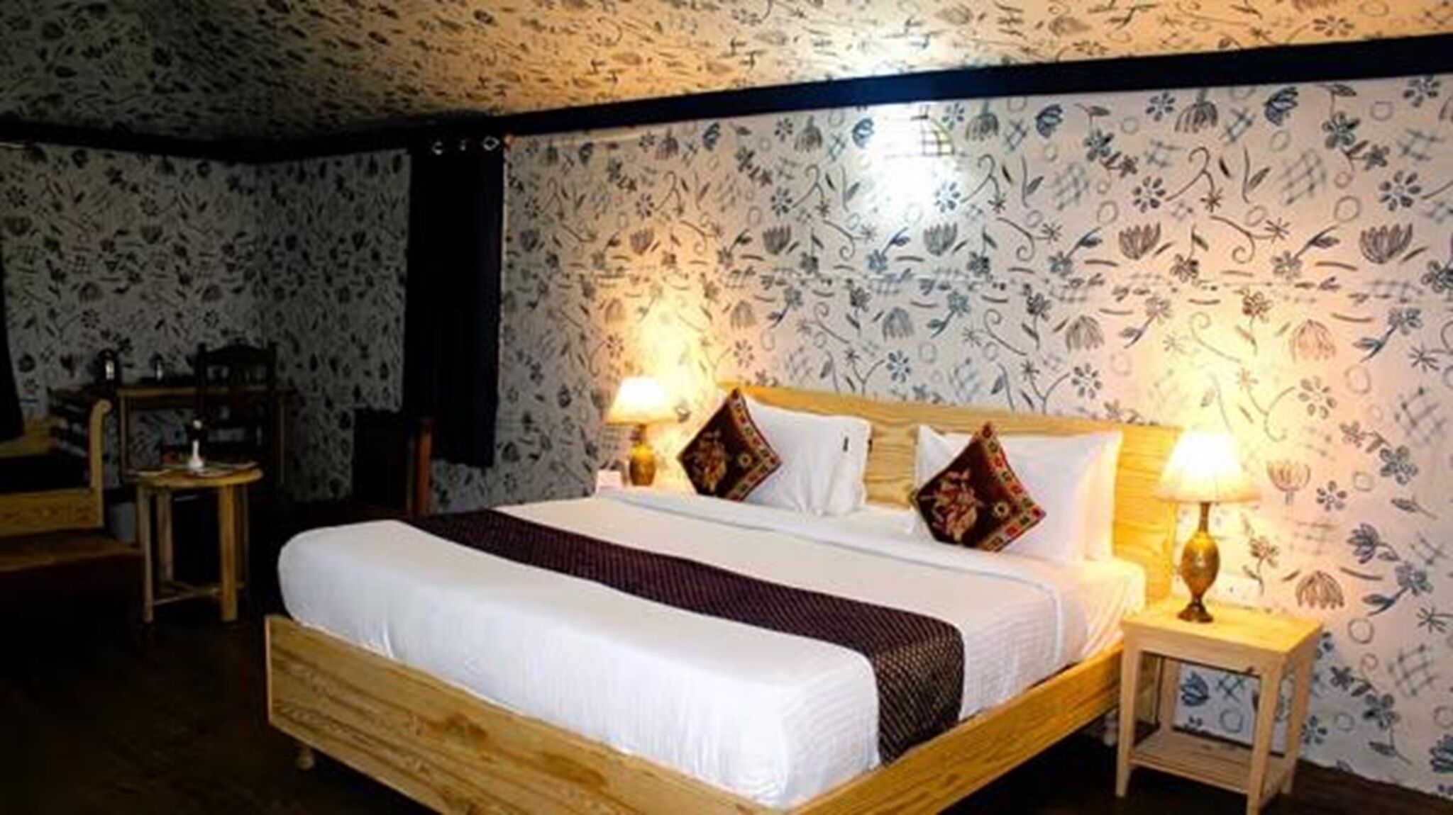 A hotel room with a wooden bed, two bedside lamps, and floral wallpaper.