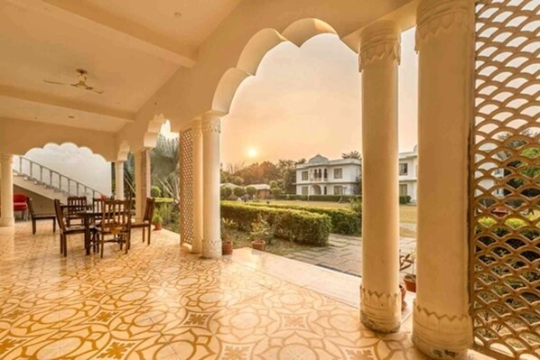 A covered outdoor area with patterned flooring, columns, and a view of a building in the background. - Clarks Inn Suites Ranthambore (Sawai Madhopur)