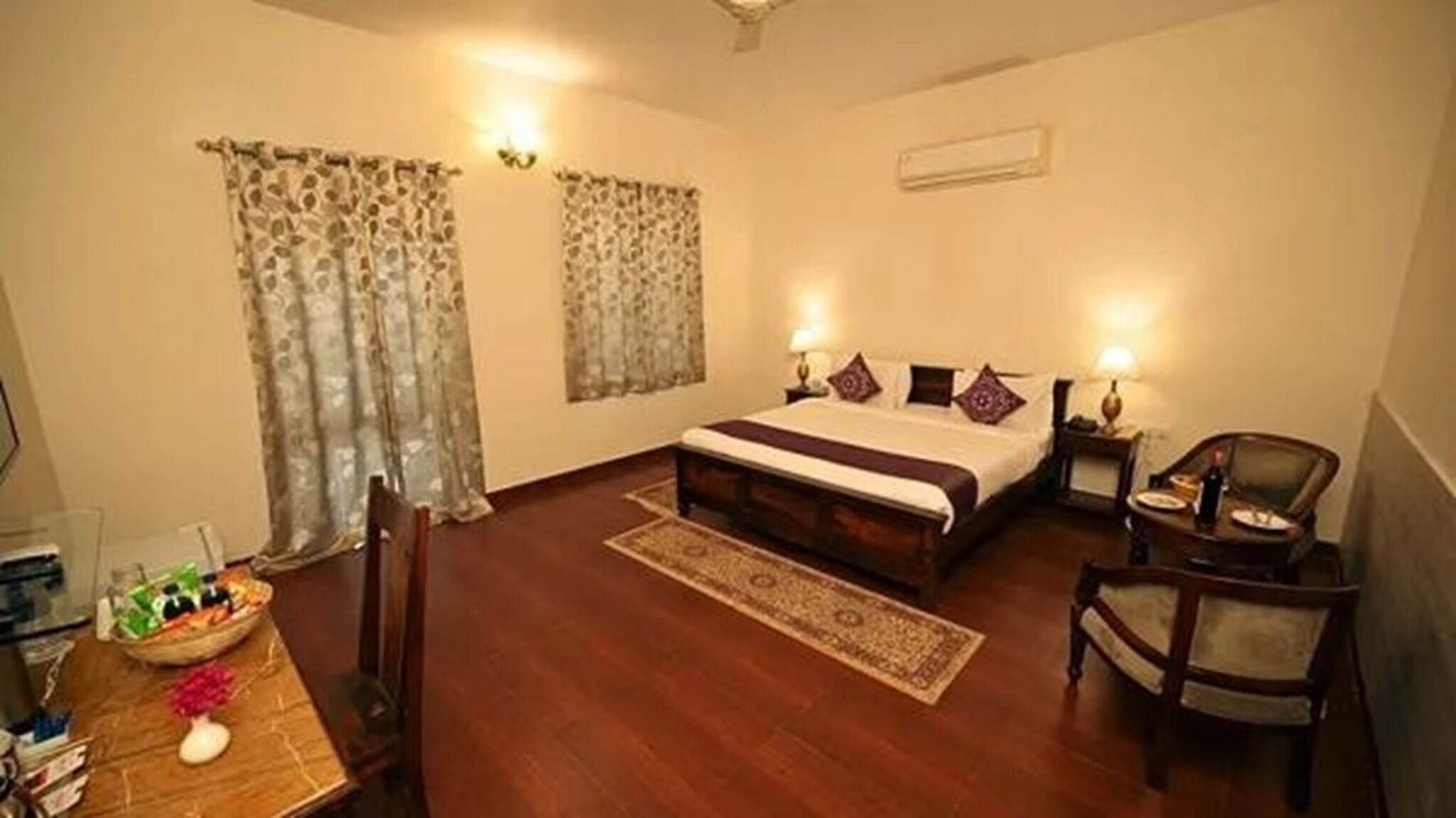 A hotel room with a bed, a chair, a table with a vase, and curtains.