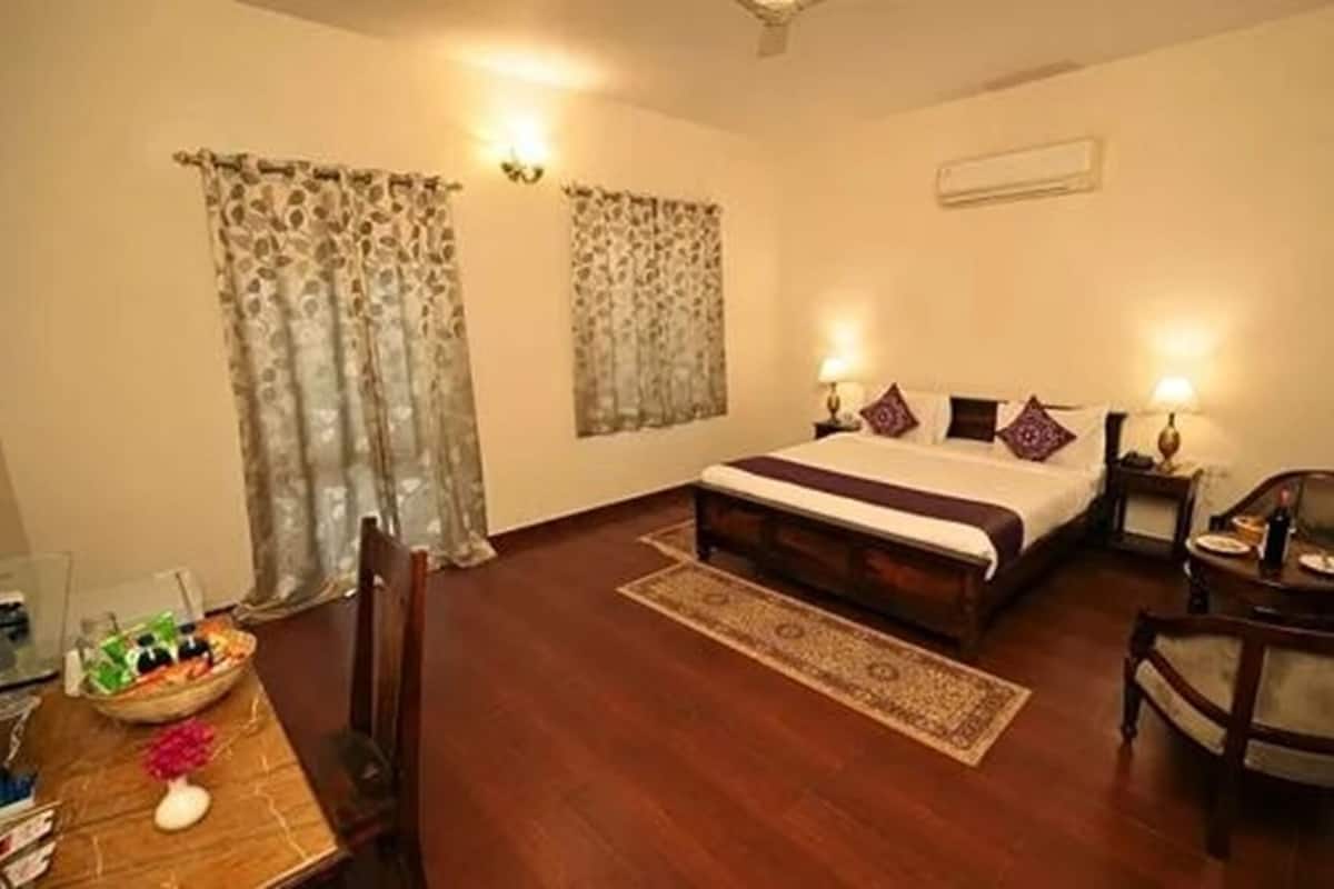 A hotel room with a bed, a chair, a table with a vase, and curtains.