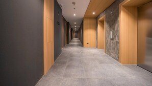 A modern hallway with a tiled floor, wooden paneling on the walls, and a series of doors leading to rooms. - Ando Hotel Batam (Batam)
