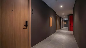 A hallway with a wooden door, a number '810' on the wall, and a red door at the end. - Ando Hotel Batam (Batam)
