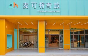 L’entrée d’un hôtel avec un local à vélos et une enseigne indiquant un service de réparation/dépôt de vélos.